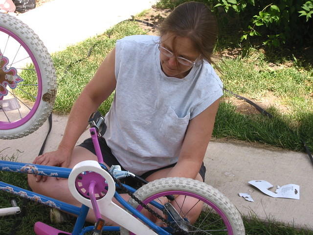 Mom attaching a kickstand to Carrie's bike.