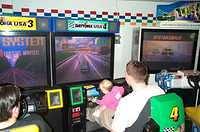 Carrie playing a racing game, on Jason's lap, at Chuck E Cheese